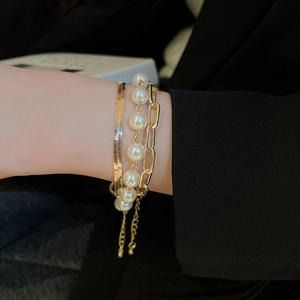 Close-up of gold layered bracelet set with pearls and paperclip chain on a model's wrist