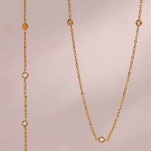 Macro detail of gold thin chain necklace featuring multiple round bezel-set clear crystals