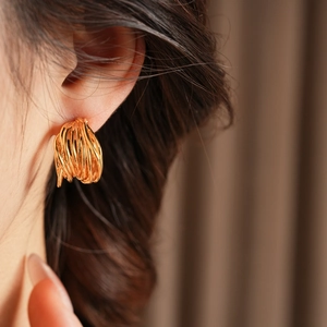 Macro view of gold plated multi-layer wrapped C-shaped earrings on model's ear