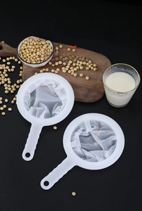 Fine mesh kitchen strainer with handle shown filtering fresh soy milk on dark background