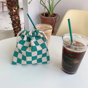 Bolsa de cuadros verdes y crema con cordón ajustable en un ambiente de cafetería