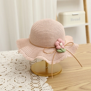 Close-up of pink straw sun hat for girls with floral decoration and wavy brim detail