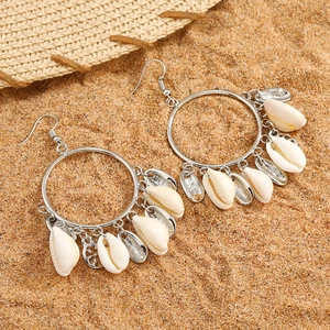 Detailed view of silver hoop earrings with natural white shells on beach sand backdrop