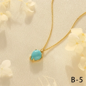 Detail of 18K gold-plated cuban chain with blue teardrop gemstone pendant on beige silk