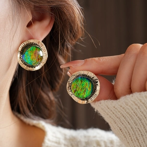 Close-up of vintage gold round earrings with blue-green opal stones worn by a model