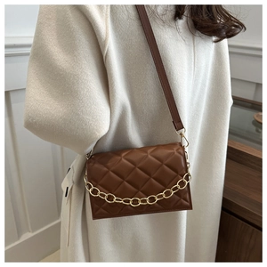 Close-up of brown quilted faux leather shoulder bag with gold chain and strap on a model