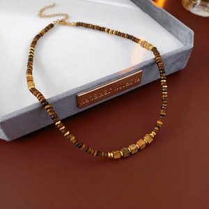Detail of square tiger eye stone necklace with gold beads on grey velvet jewelry tray
