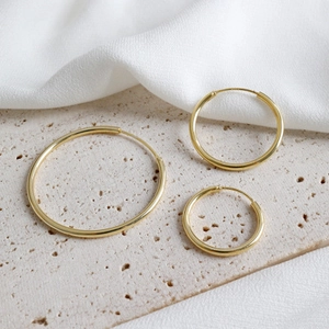 Three sizes of gold minimalist S925 sterling silver hoop earrings on stone background