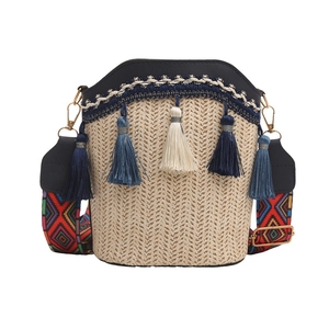 Detail of woven straw bucket bag with blue tassels and colorful geometric fabric strap