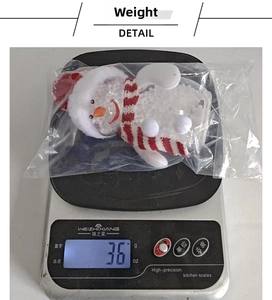Close-up of a glowing snowman ornament with red hat on a scale showing 36g weight