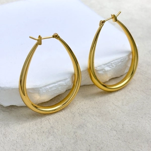 Polished gold teardrop hoop earrings in minimalist style on white stone display