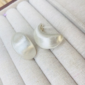 Vue macro de boucles d'oreilles croissant en argent mat brossé sur une boîte en tissu beige