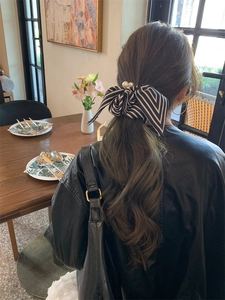 Detail of striped bow hair scrunchie with pearl accent on a high ponytail style