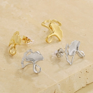 Detail view of ginkgo leaf stud earrings in gold and silver finishes on stone background