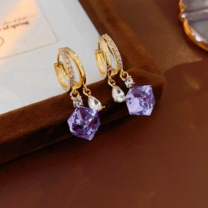 Detail of luxury gold earrings with square purple zircon and clear teardrop crystal pendants