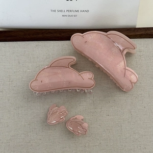 Pink dolphin-shaped hair clips in various sizes with glitter finish on fabric background