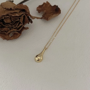 Detailed close-up of a minimalist golden teardrop pendant on a fine link chain necklace
