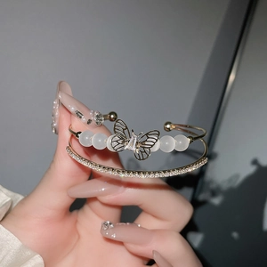 Detail eines goldfarbenen Armbands mit Opalperlen und Kristall-Schmetterlingsanhänger