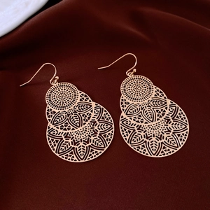 Detailed macro view of gold hollow-out floral pattern earrings on red velvet cloth