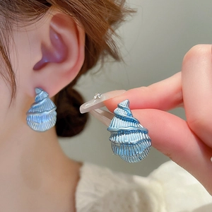 Vue détaillée de petites boucles d'oreilles en forme de coquillage bleu sur un mannequin