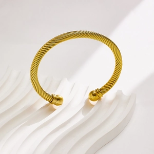 Gold stainless steel twisted cable bangle with round beads on white stone pedestal