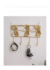 Detail of golden ginkgo leaf wall hook holding a watch and keys on a white wall