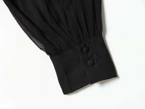 Detalle de mangas farol traslúcidas con puños de doble botón en camisa negra elegante
