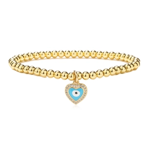 Detail of golden beaded bracelet with heart charm featuring a blue evil eye and crystals
