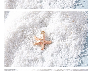 Detail of pink starfish charm with gold metal edges on white sand beach background