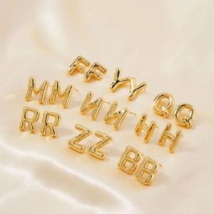 Macro detail of various golden letter stud earrings on champagne silk background