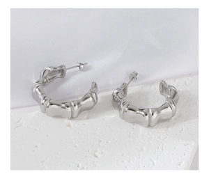 Detailed view of silver bamboo joint C-shape earrings on a white textured rock base