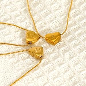 Golden titanium steel heart pendant necklaces with letters A, B, and C on woven fabric