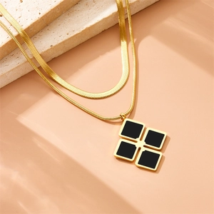 Detail of a double-layered gold chain necklace with a black geometric square pendant