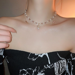 Close-up of double-layer gold necklace with pearls and purple crystal on model neck