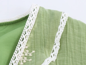 Macro shot of green textured fabric with white floral lace trim and embroidery detail