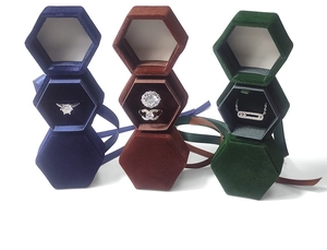 Three-tier stack of hexagonal velvet jewelry boxes with ribbons in green, blue, and brown