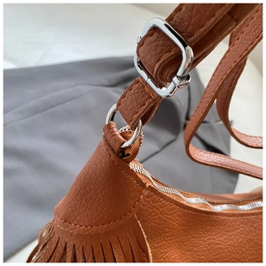 Detail of brown leather bag showing tassel design and silver metal strap buckle