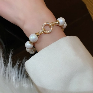 Close-up of white pearls and a gold diamond-encrusted ring clasp on a woman's wrist