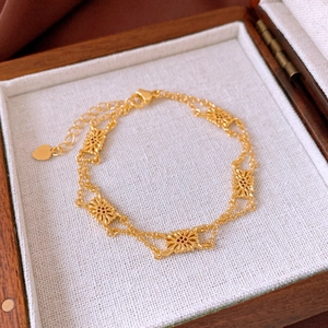 Detail of double-layer gold bracelet with hollow flower motifs on linen texture