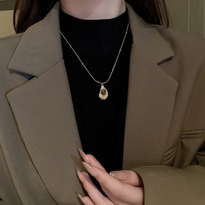 Close-up of a gold snake chain necklace with a faux tiger eye pendant on a model