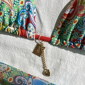 Detail of bikini top with paisley print, gold chain, heart charm and metal logo tag