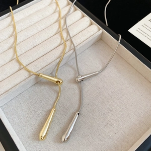 Close-up of gold and silver teardrop pendants on snake chains in a jewelry box