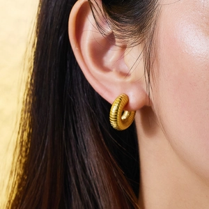 Detail of gold-plated hoop earrings with fine horizontal ribbed texture on earlobe