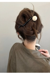Détail d'un pic à cheveux noir minimaliste avec perle blanche sur une coiffure relevée