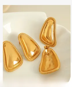 Detail of 18K gold plated geometric ear studs with polished texture in a white dish