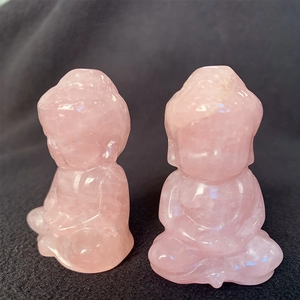 Detailed view of two small hand-carved pink crystal Buddha statues on a grey fabric base
