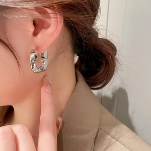 Gros plan d'une boucle d'oreille géométrique en argent en forme de U portée par un modèle