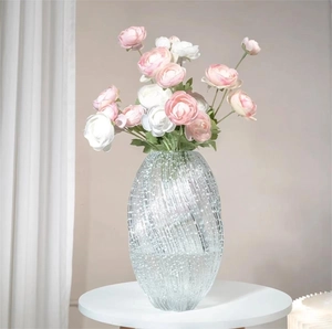 Luminous glass flower vase with bubble texture and pink ranunculus on a white table