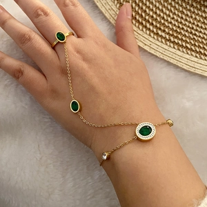 Detailed close-up of gold hand chain with emerald green gemstone and zircon accents