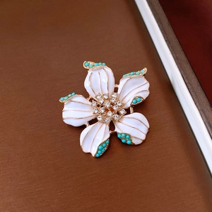 Detail showing white enamel flower brooch with gold edges and crystal center